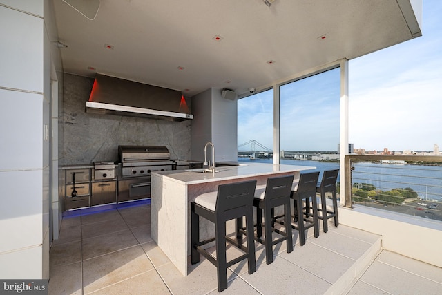 kitchen featuring light tile patterned floors, wall chimney exhaust hood, a water view, a kitchen bar, and a sink