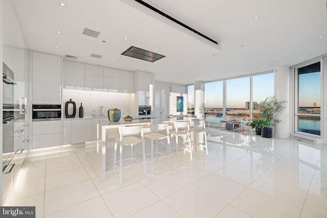 kitchen featuring a sink, stainless steel oven, decorative backsplash, a wall of windows, and modern cabinets