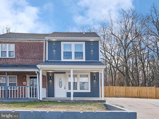 view of front of property with roof with shingles, fence, a porch, and brick siding