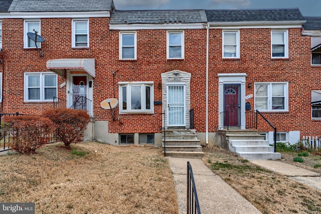 townhome / multi-family property featuring brick siding, mansard roof, a shingled roof, entry steps, and a front lawn