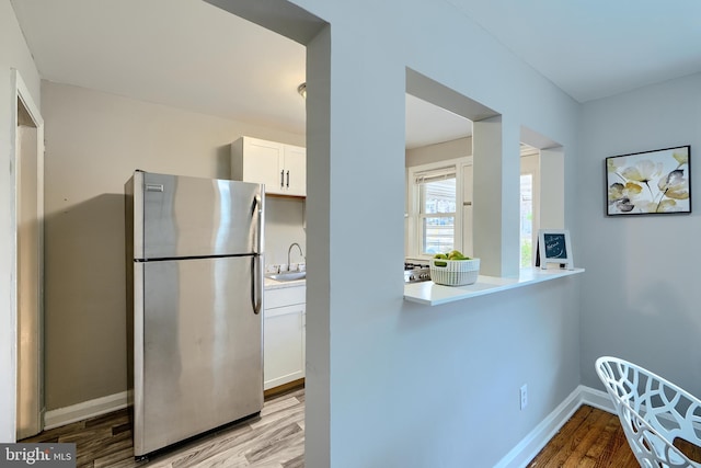 kitchen with light wood finished floors, white cabinets, freestanding refrigerator, light countertops, and a sink