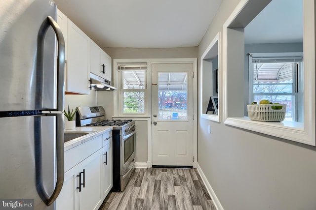 kitchen with stainless steel appliances, plenty of natural light, white cabinets, and under cabinet range hood