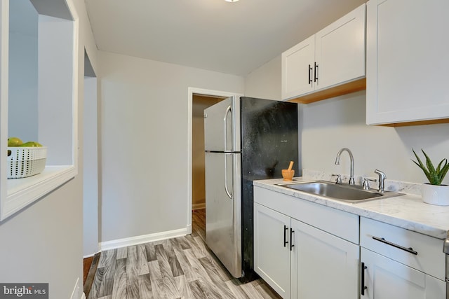 kitchen featuring a sink, baseboards, white cabinets, light wood-type flooring, and freestanding refrigerator