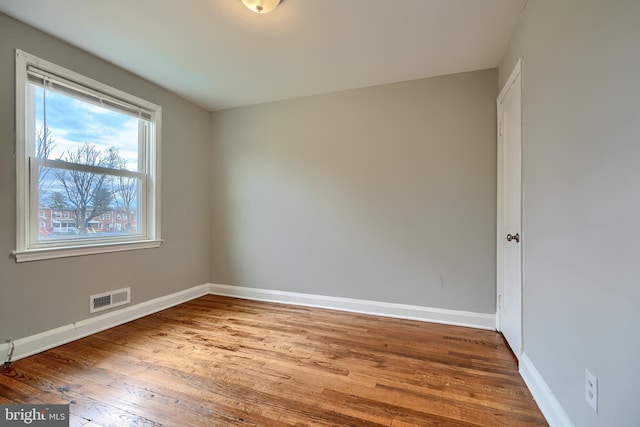 spare room with baseboards, visible vents, and wood finished floors