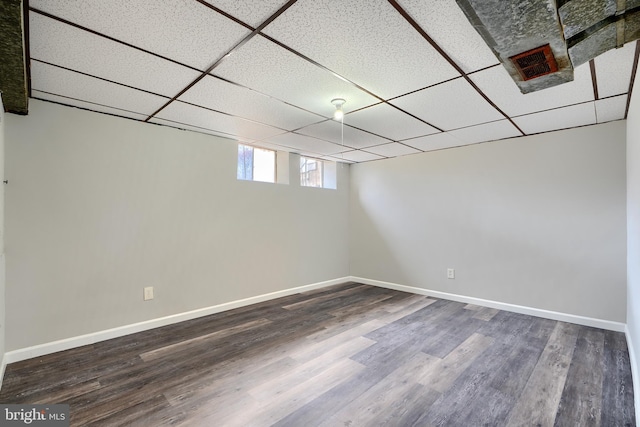 basement with a drop ceiling, dark wood finished floors, visible vents, and baseboards