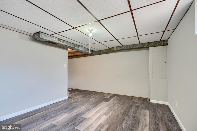 finished basement featuring concrete block wall, a paneled ceiling, baseboards, and wood finished floors