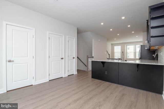 kitchen featuring a kitchen bar, light stone counters, recessed lighting, light wood-style flooring, and a peninsula