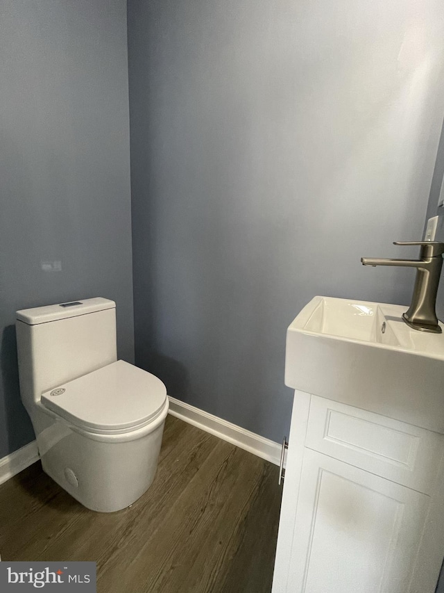 half bath with toilet, baseboards, and wood finished floors