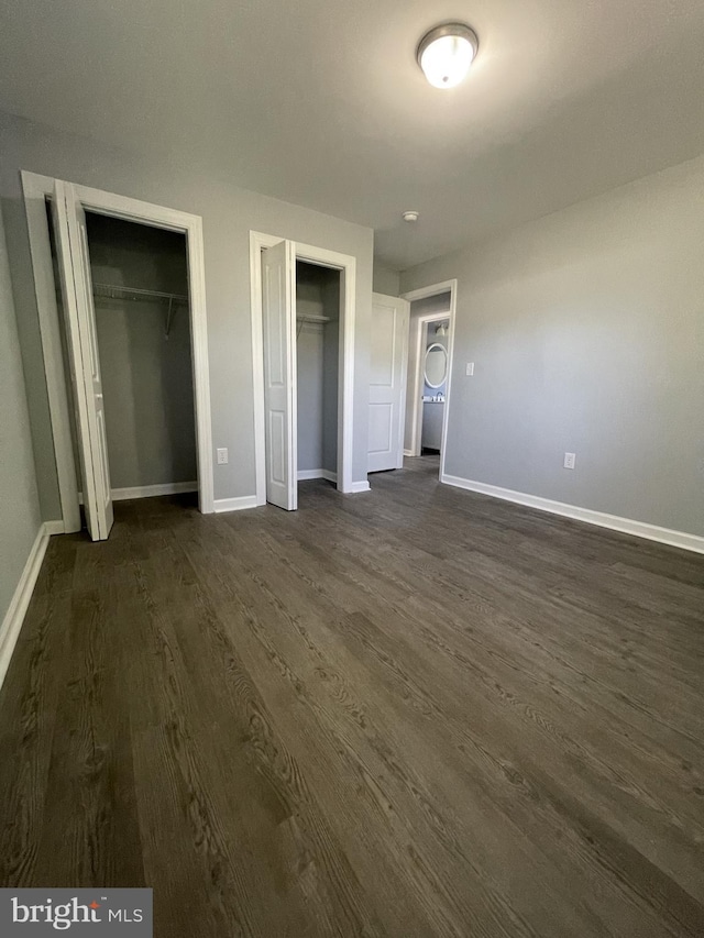 unfurnished bedroom with baseboards, dark wood finished floors, and two closets