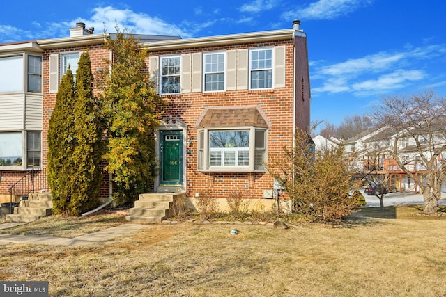 multi unit property with brick siding, a chimney, and a front lawn