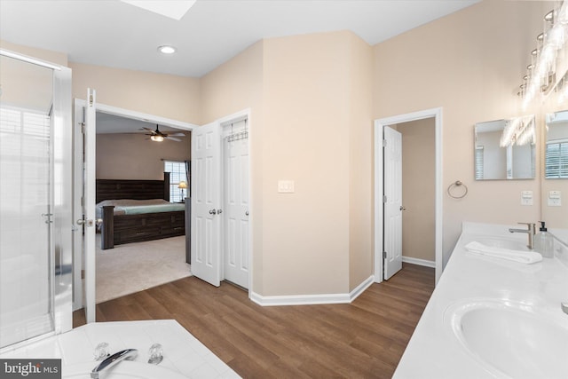 ensuite bathroom featuring a stall shower, a sink, ensuite bath, wood finished floors, and double vanity