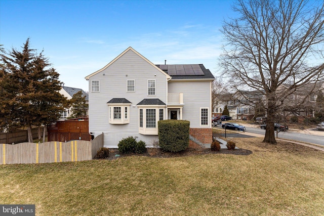 back of house featuring a yard, fence, roof mounted solar panels, and roof with shingles