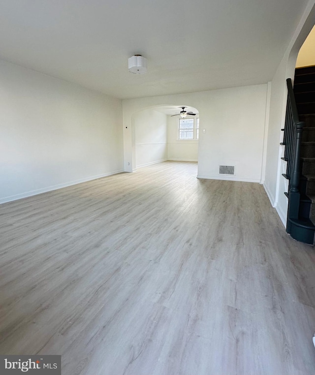 empty room with arched walkways, visible vents, a ceiling fan, wood finished floors, and stairs