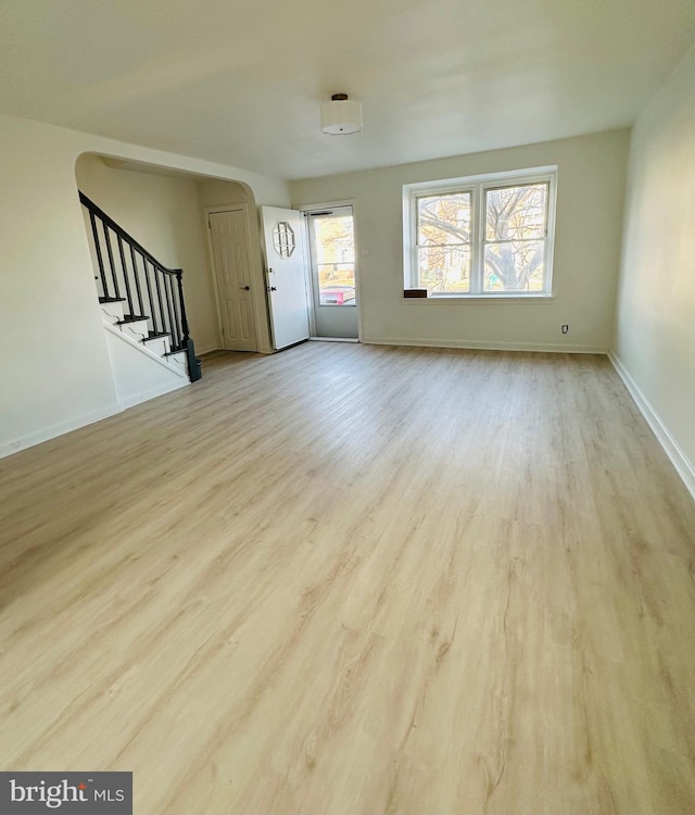 unfurnished living room featuring stairs, baseboards, arched walkways, and wood finished floors