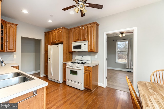 kitchen featuring light countertops, light wood-style floors, a sink, white appliances, and baseboards