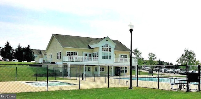 rear view of house featuring a balcony, a lawn, fence, and a fenced in pool