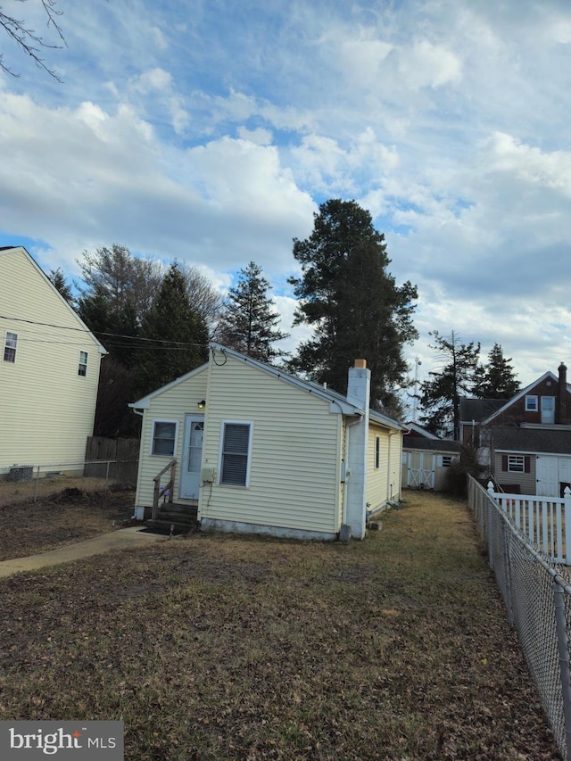 rear view of property featuring entry steps, a fenced backyard, a lawn, and a chimney