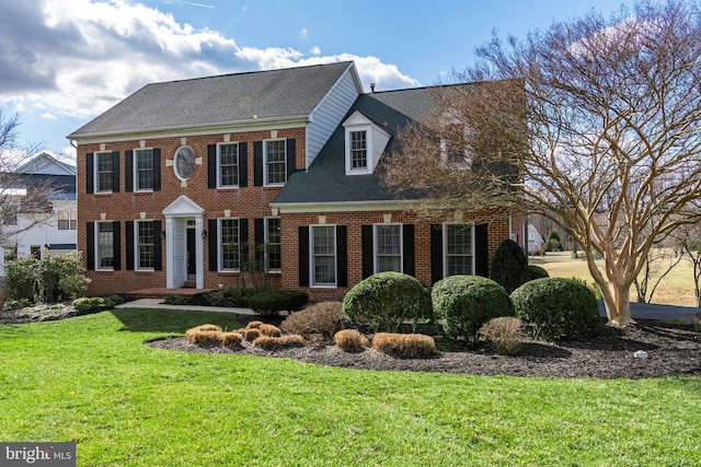 colonial inspired home with a shingled roof, brick siding, and a front lawn