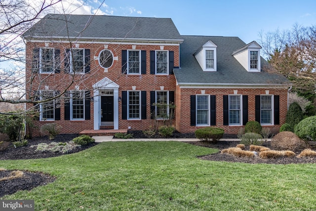 georgian-style home featuring brick siding, a front lawn, and roof with shingles