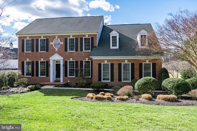 colonial-style house with brick siding, a front yard, and a shingled roof