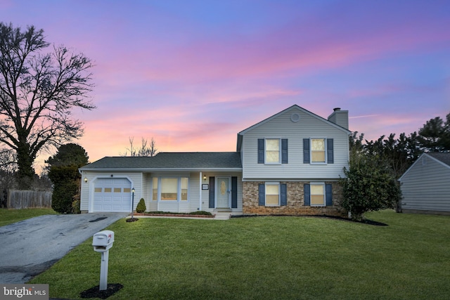 split level home featuring aphalt driveway, an attached garage, brick siding, and a front yard