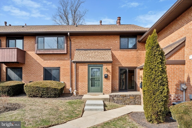 view of front of property featuring brick siding and roof with shingles