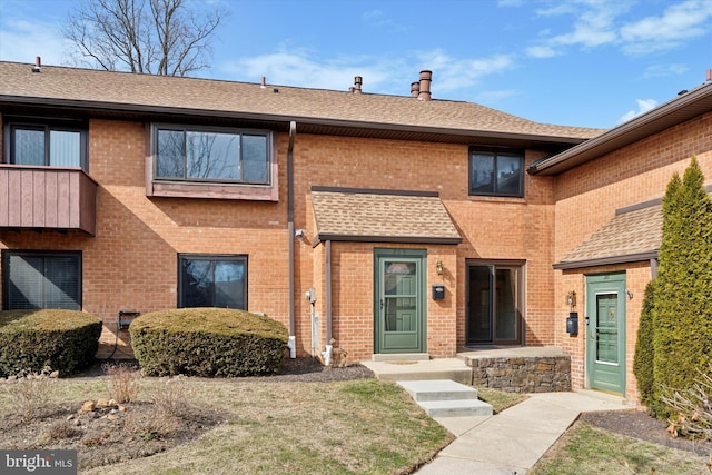 view of front facade featuring roof with shingles and brick siding