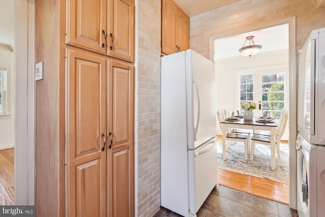 kitchen featuring stacked washing maching and dryer, tile patterned flooring, and freestanding refrigerator