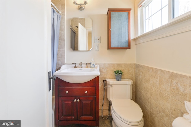 bathroom with toilet, a wainscoted wall, curtained shower, vanity, and tile walls