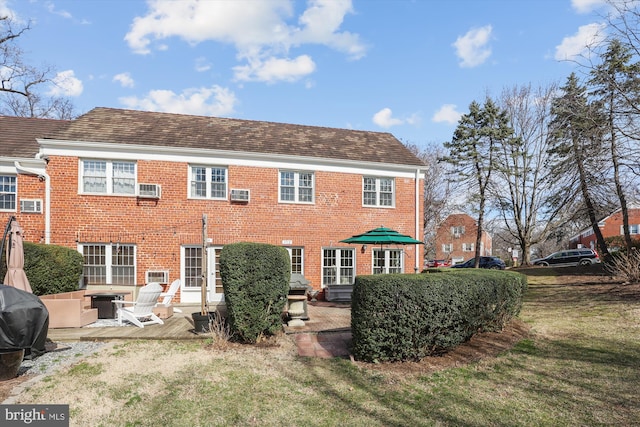 rear view of house featuring a yard, brick siding, roof with shingles, and a patio area