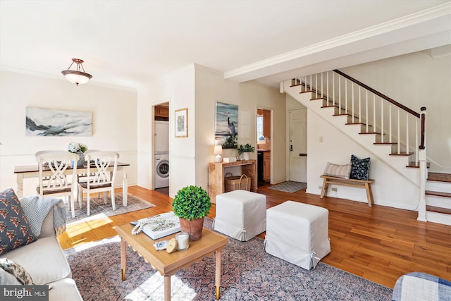 living room with baseboards, stairway, hardwood / wood-style floors, stacked washer / drying machine, and crown molding