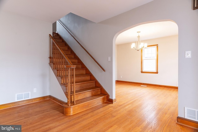 staircase featuring arched walkways, visible vents, and wood finished floors