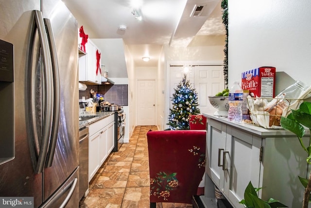 kitchen featuring stainless steel appliances, visible vents, white cabinets, backsplash, and stone finish floor