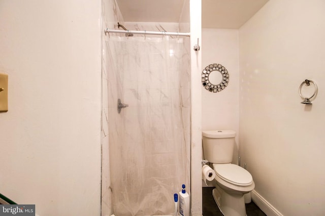 full bathroom featuring baseboards, a tile shower, and toilet