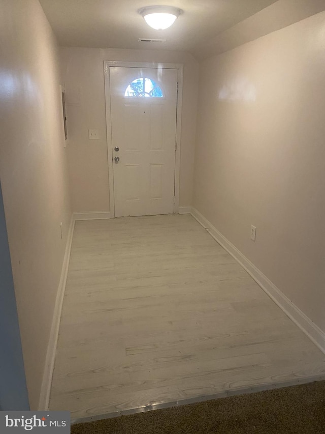 doorway with light wood-style floors, visible vents, and baseboards