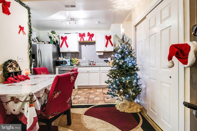 kitchen with tile countertops, visible vents, decorative backsplash, white cabinets, and stainless steel fridge with ice dispenser