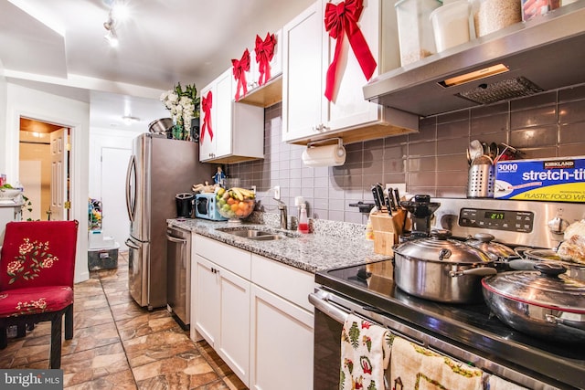 kitchen featuring tasteful backsplash, appliances with stainless steel finishes, white cabinetry, a sink, and wall chimney exhaust hood