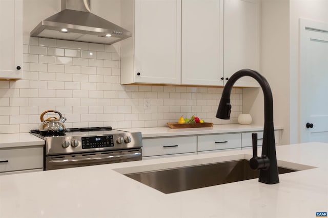 kitchen featuring stainless steel electric stove, a sink, light countertops, decorative backsplash, and wall chimney exhaust hood