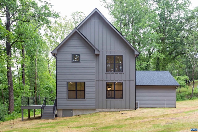 rear view of house featuring roof with shingles, a deck, board and batten siding, and a yard