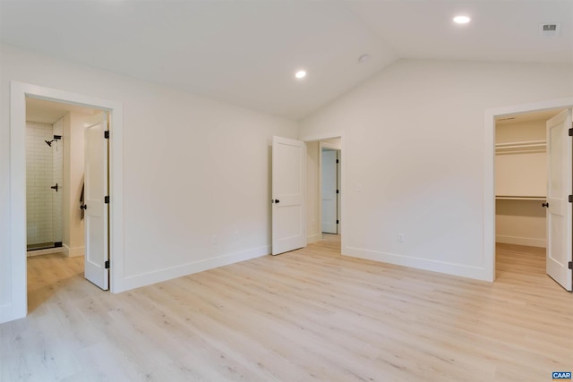 unfurnished bedroom featuring vaulted ceiling, a spacious closet, light wood-style flooring, and baseboards