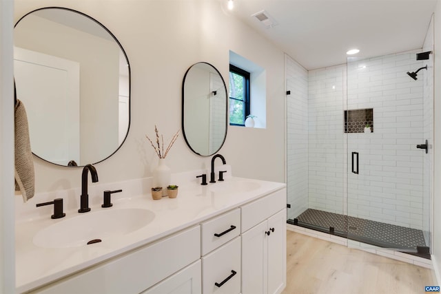 bathroom featuring wood finished floors, a sink, visible vents, and a shower stall