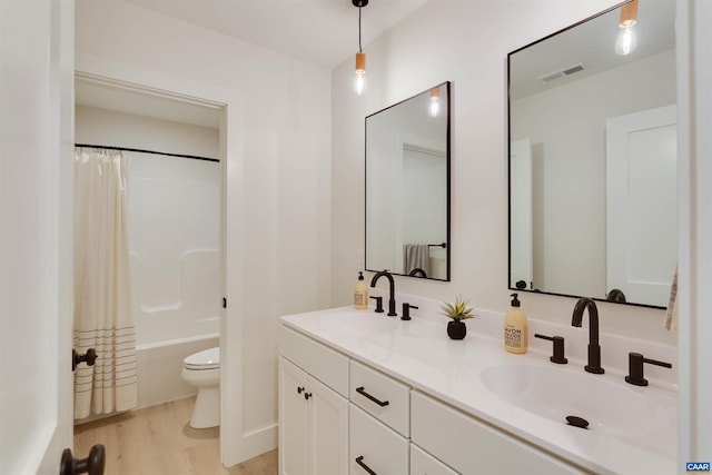 bathroom featuring toilet, double vanity, a sink, and wood finished floors