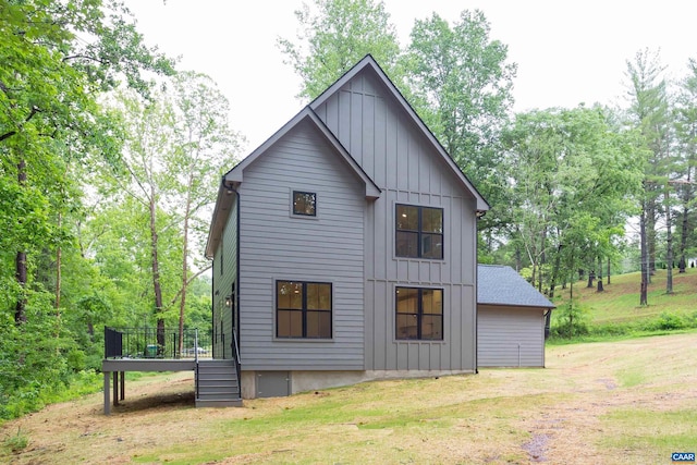 rear view of property featuring a deck, a shingled roof, board and batten siding, and a lawn