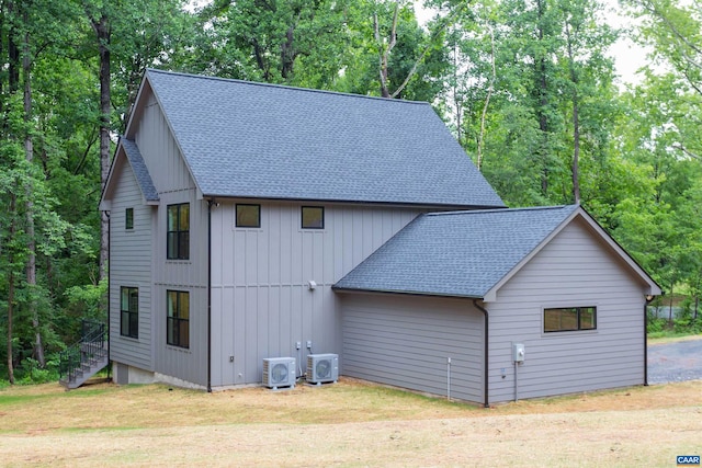 view of home's exterior featuring ac unit, a shingled roof, a lawn, and board and batten siding