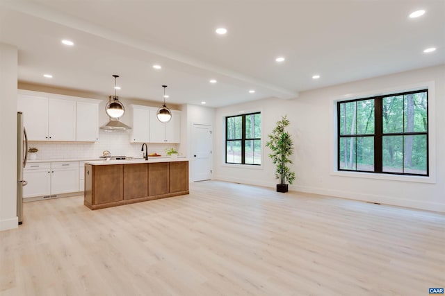 kitchen with light wood-style flooring, light countertops, backsplash, freestanding refrigerator, and an island with sink