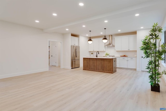 kitchen with light wood-style flooring, a sink, wall chimney range hood, decorative backsplash, and stainless steel fridge