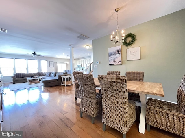 dining space with wood-type flooring, visible vents, stairway, and ceiling fan with notable chandelier