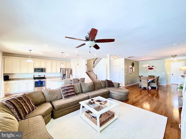 living room with stairs, a ceiling fan, baseboards, and hardwood / wood-style flooring