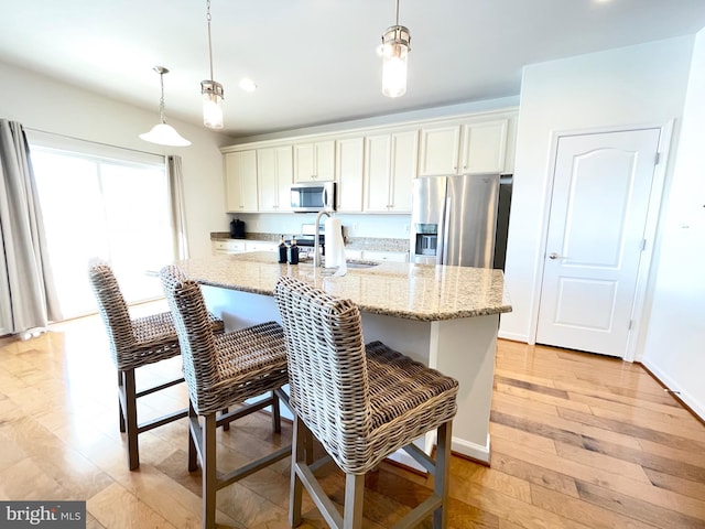 kitchen featuring stainless steel appliances, a kitchen bar, a kitchen island with sink, and decorative light fixtures