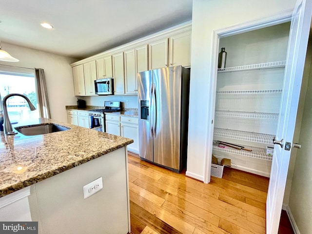 kitchen with light wood finished floors, appliances with stainless steel finishes, light stone countertops, a sink, and recessed lighting